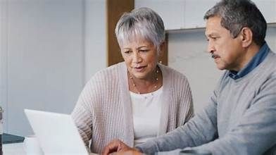 Two individuals sitting at a table, one using a laptop while the other observes attentively.