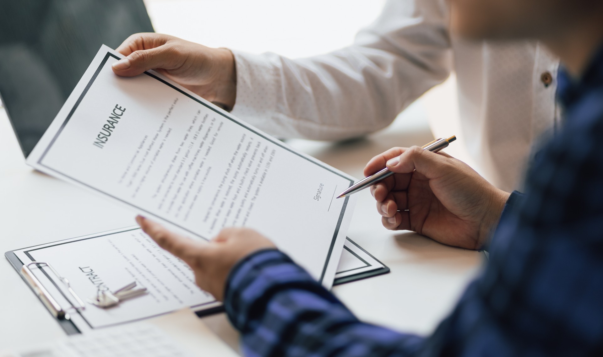 Man in office showing an insurance policy and pointing with a pen where the policyholder must to sign. Insurance agent man presentation and consulting insurance terms detail to customer and waiting for his signing.