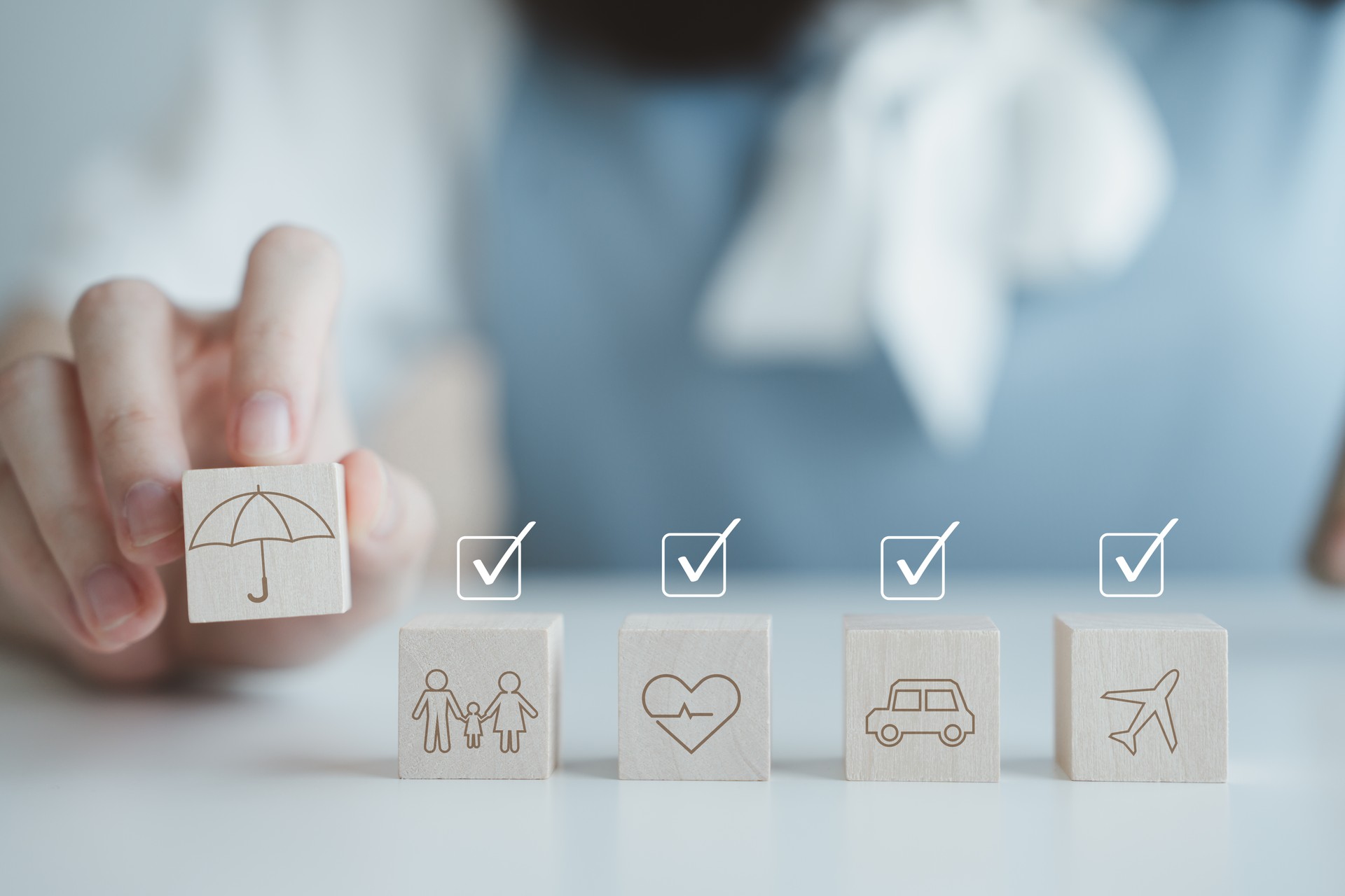 Insurance concept. Protection against a possible eventuality. Hand holding umbrella icon for security symbol and car, family, travel and health on wooden block with check mark. Life assurance concept.